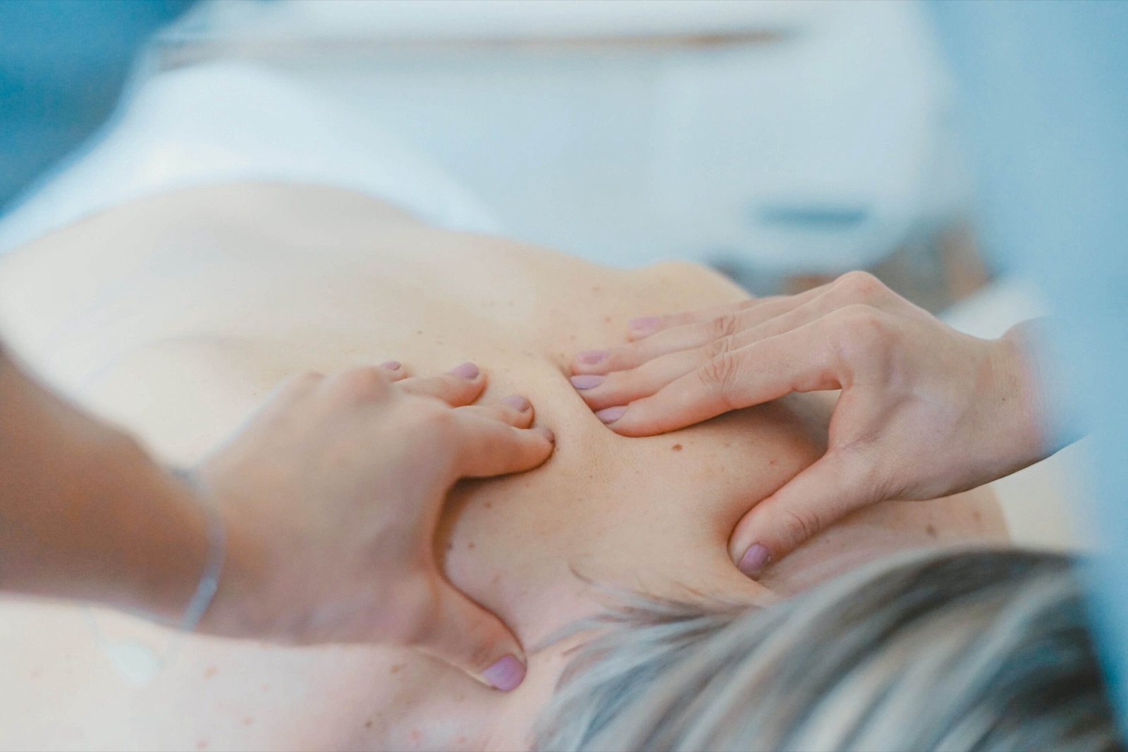 Massageterapeutens händer arbetar med spända muskler i övre ryggen